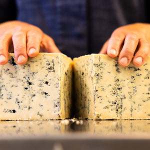 Hands opening up a wheel of Bay Blue cheese