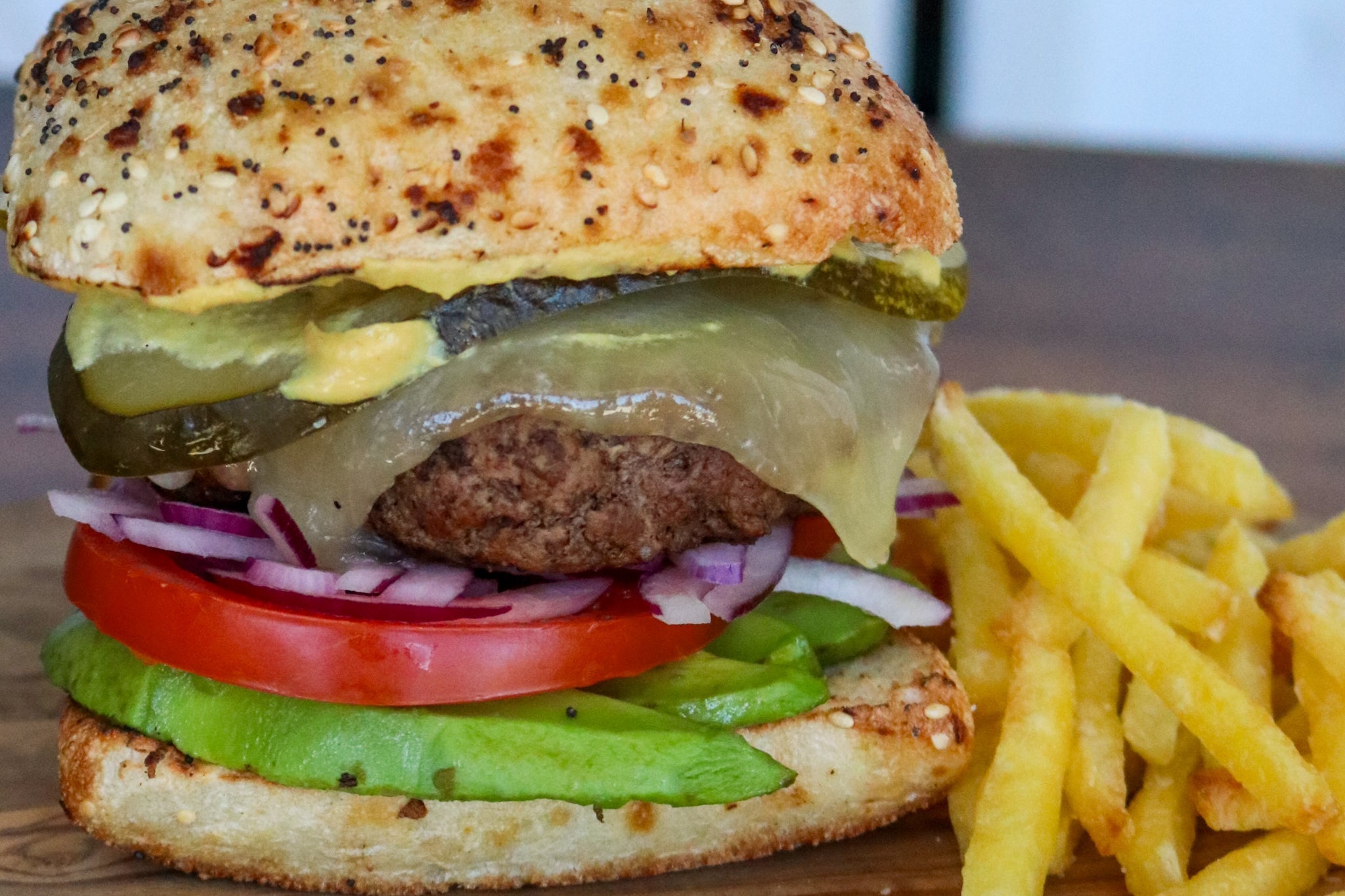 burger with melted toma, pickles, avocado, tomato on a seeded bun