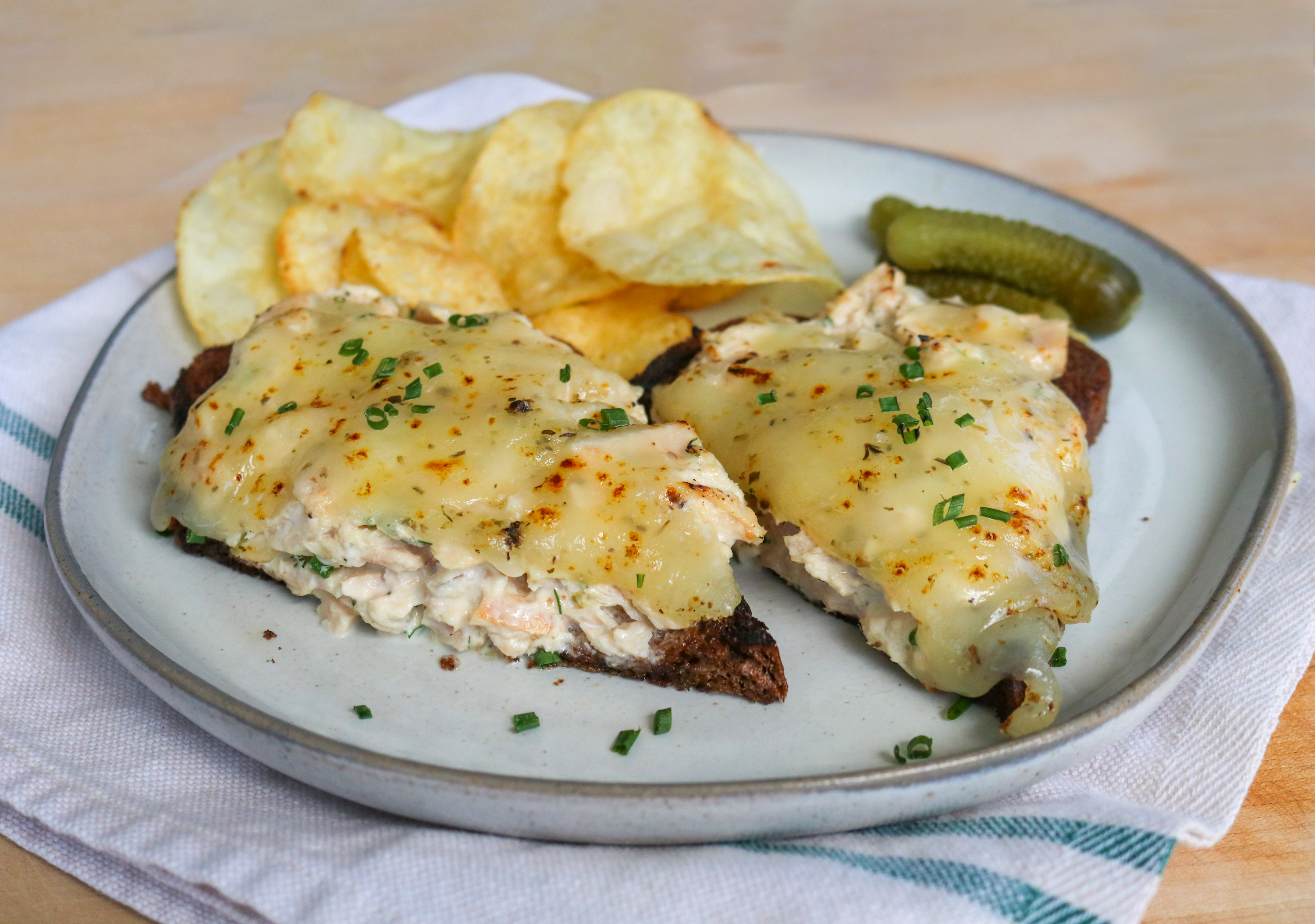 open faced tuna melt on a plate with chips and pickles