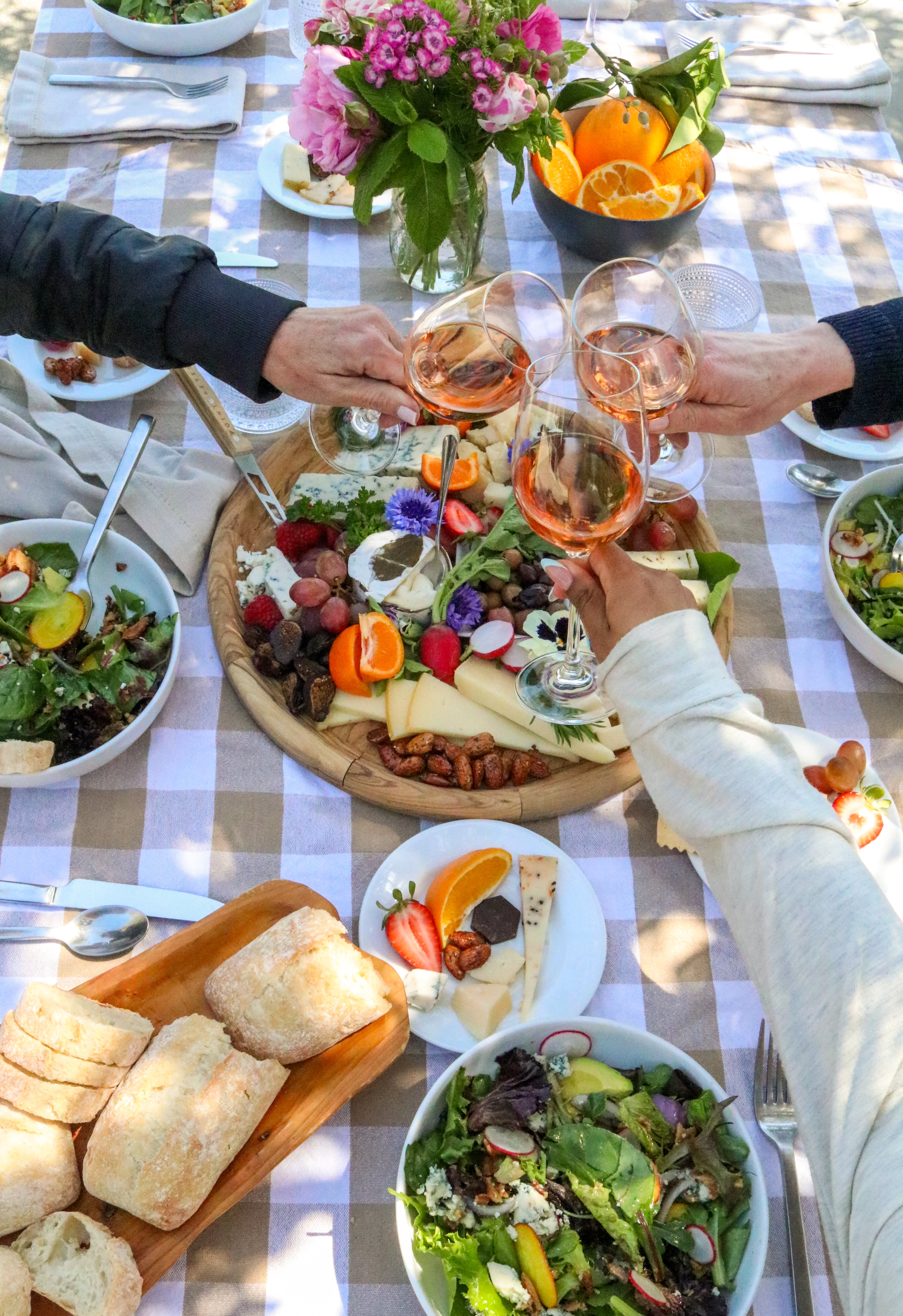 People toasting with wine glasses at a table set with food and drinks.