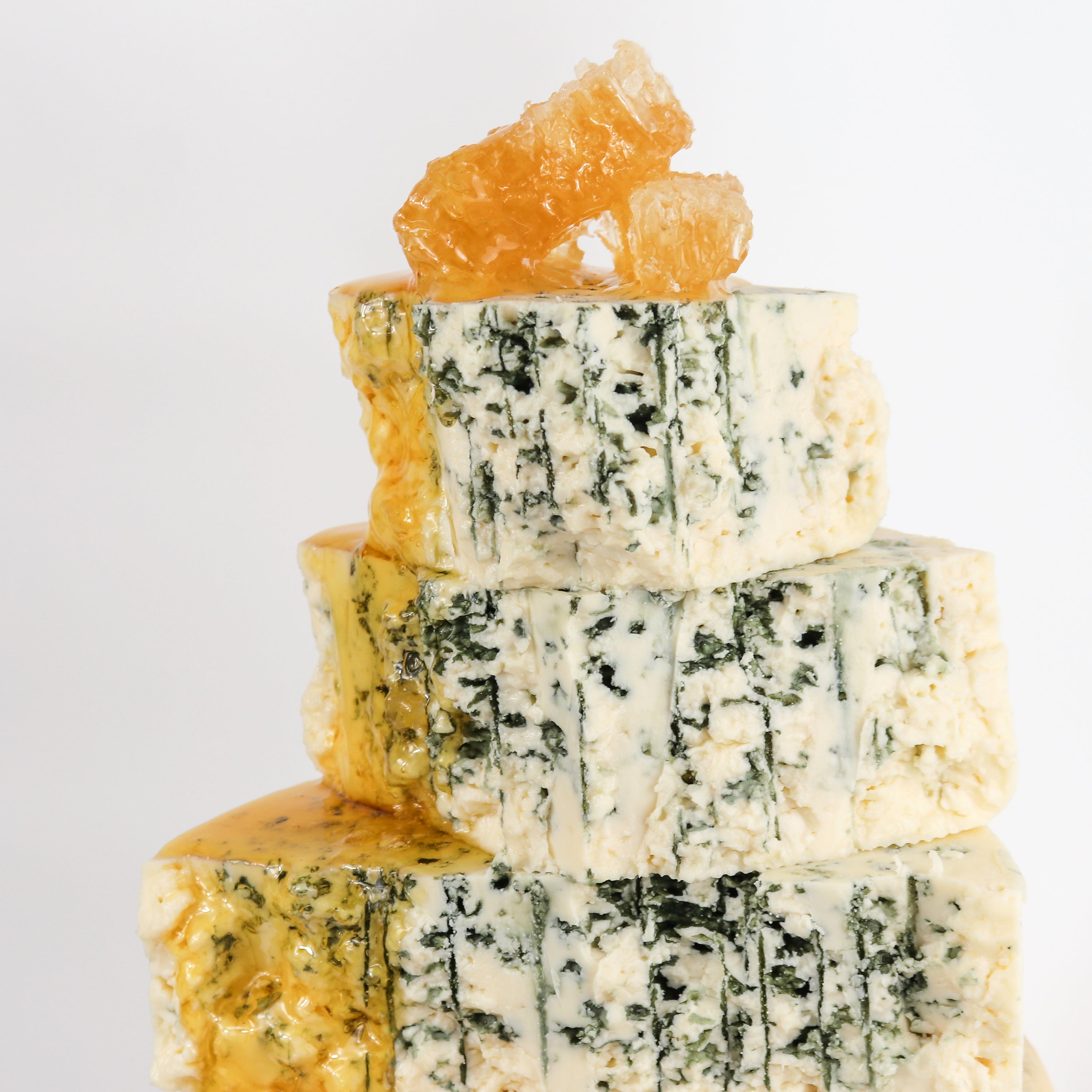 Pieces of Original Blue cheese with honeycomb on top and honey dripping down the side