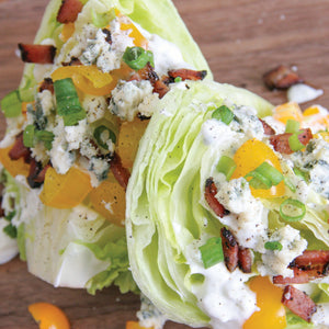 A Wedge salad topped with bacon, tomatoes, gren onions, and Original Blue cheese dressing